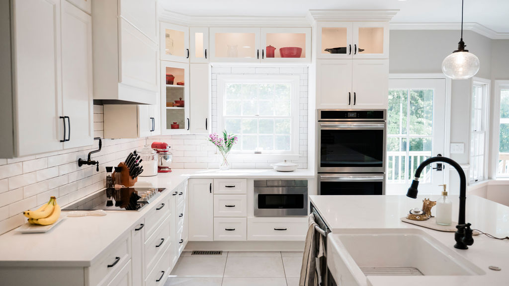 White kitchen with shaker cabinetry, large island sink, subway tile backsplash, and built-in stainless steel appliances.
